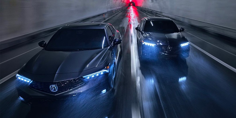 Two sleek 2025 Acura Integra sedans with bright headlights speeding through a tunnel. The background is blurred.