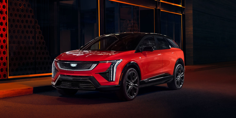 A shiny red electric 2025 Cadillac OPTIQ SUV parked at night, highlighting its modern design and headlights.