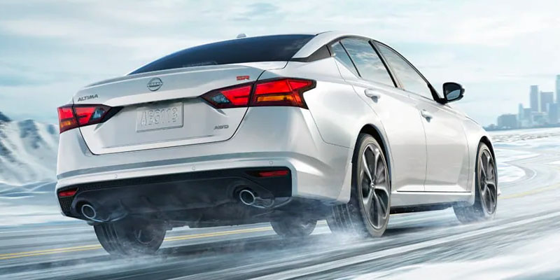 A white 2025 Nissan Altima SR driving on a snowy road, showcasing its sporty design.
