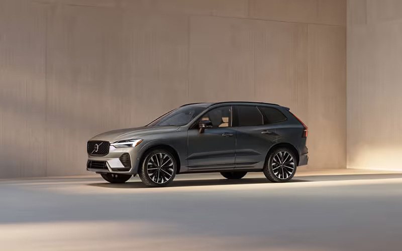 A side profile of a dark grey Volvo XC60 luxury SUV parked in a minimalist studio with warm, soft lighting.