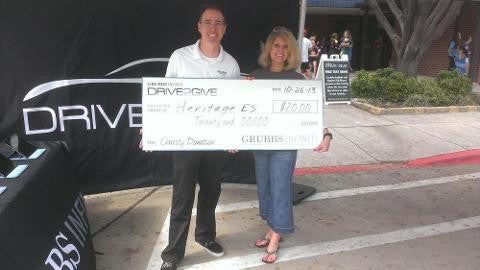 two people holding grubbs drive2give cheque near a car